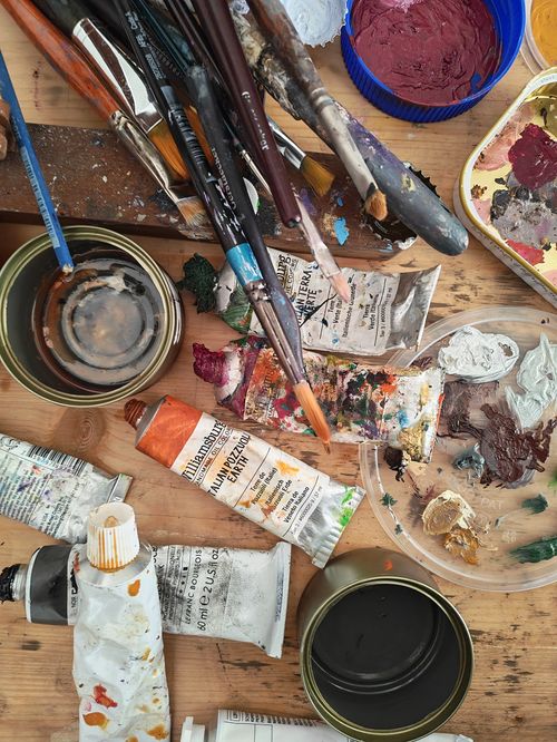 A painting of two women sitting on the ground. t tubes, brushes, mixing paletteand easel.