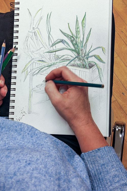 A student drawing with charcoal at a studio worktable.